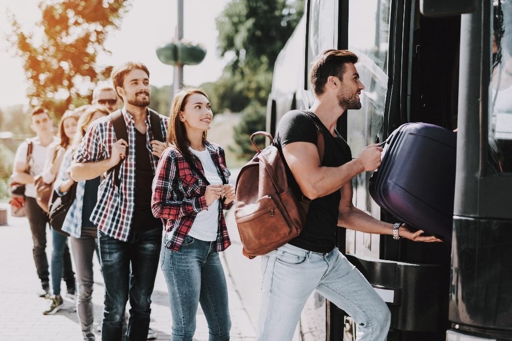 A group of people are boarding a bus with the person at the door uploading his suitcase in piece about customer onboarding and regulatory compliance.