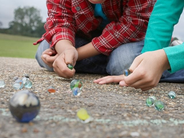 Two kids, one wearing a plaid shirt and the other wearing a turquoise shirt,, sit on the playground playing marbles in piece about CFO and marketing alignment.