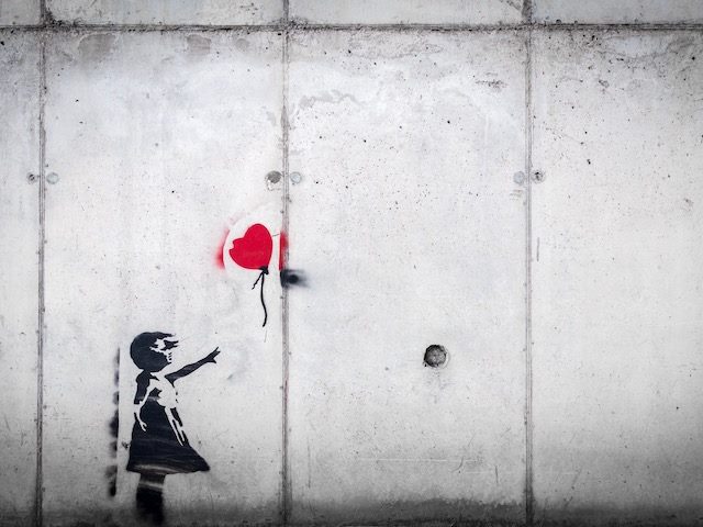 banksy or banksy  knockoff. wheatpaste grafitti art of girl on wall reaching up for a  red heart-shaped balloon