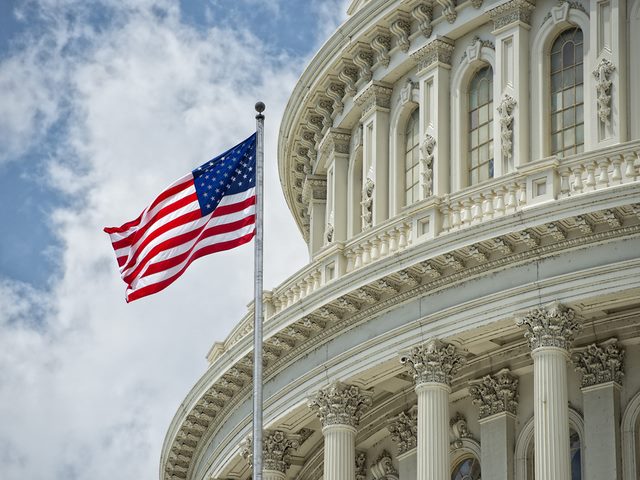 Washington DC Capitol dome with waving American flag outside.