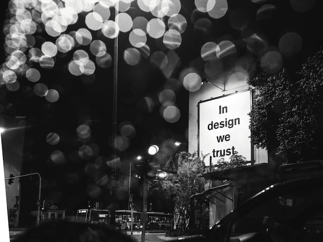a billboard reading "in design we trust" seen through a rain covered windshield