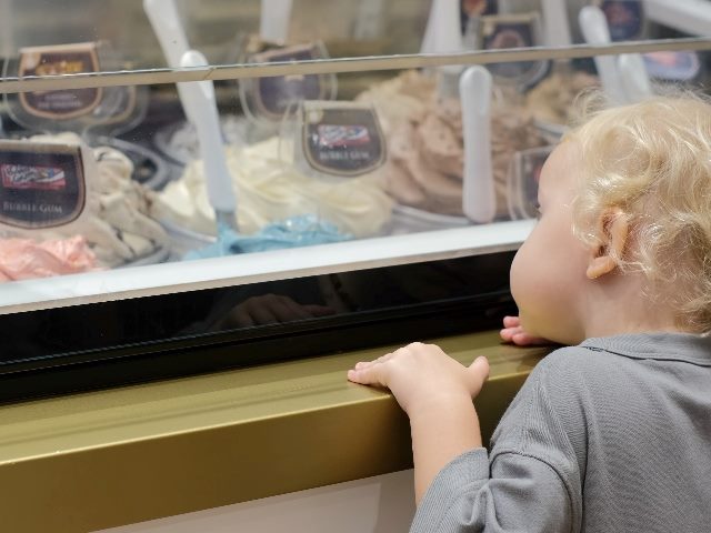 A small child with blonde hair leans against an ice cream case displaying various flavors in piece about data-driven decision-making. 