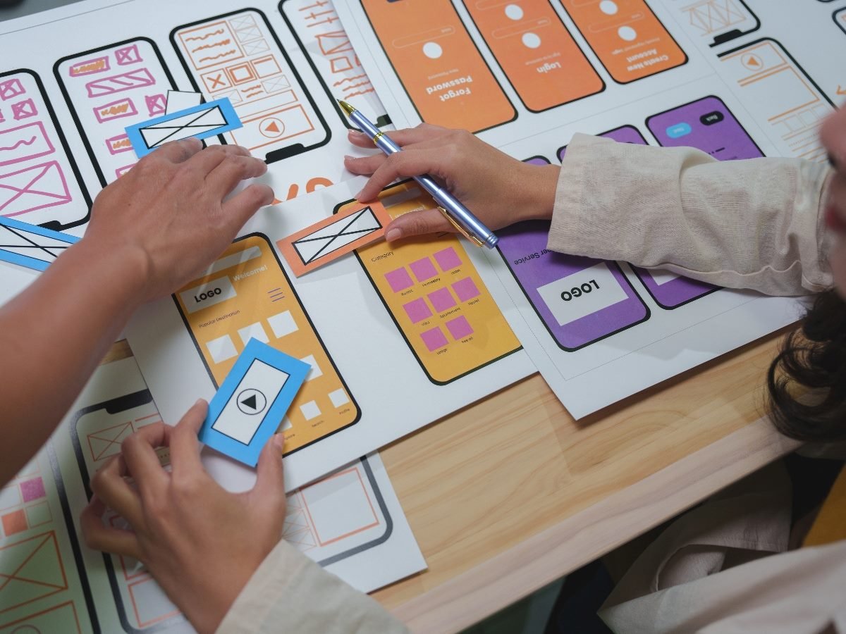 Two designers collaboratively planning a mobile app interface using paper wireframes, illustrating early-stage UX design with accessibility in mind.