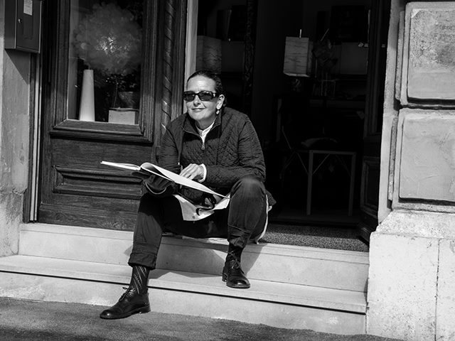 Black and white photo of a woman sitting on a stoop reading a book. 