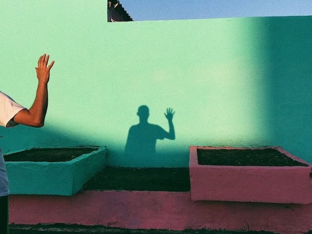 person waving hello with their  shadow waving back on a teal wall
