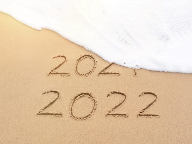 Handwritten 2021 and 2022 on sand beach with foam wave wiping out 2021. 