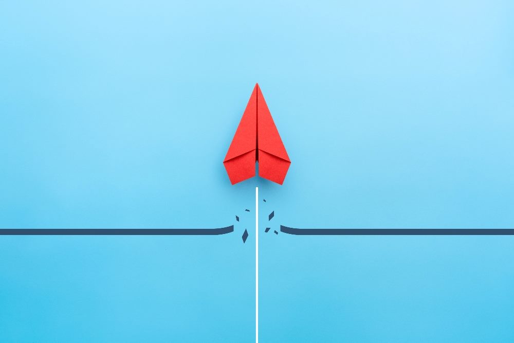 Red paper plane breaking through obstacle on blue background in piece about unified customer experience.