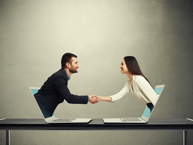 Businessman and businesswoman come out from laptop, shaking hands and looking at each other over dark grey background