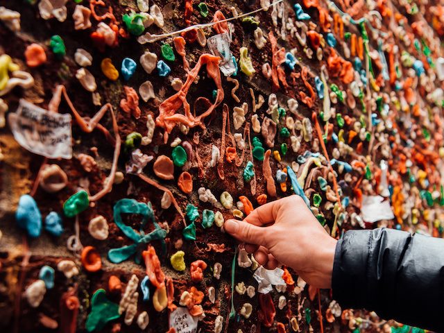 person adding some gum to a wall covered in chewing gum in Portland, Oregon