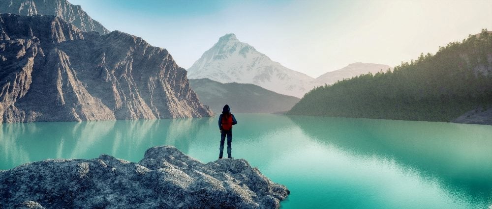 A traveler stands alone overlooking a beautiful blue lake that is reflecting the surrounding mountains in piece about customer journey orchestration.