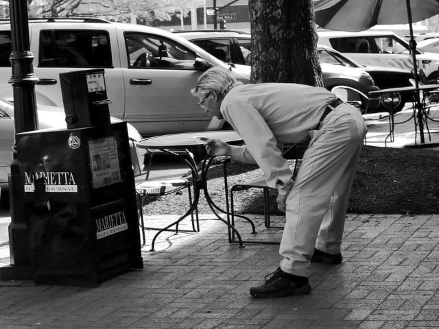 man leans over with hands on knees looking into a newspaper box.