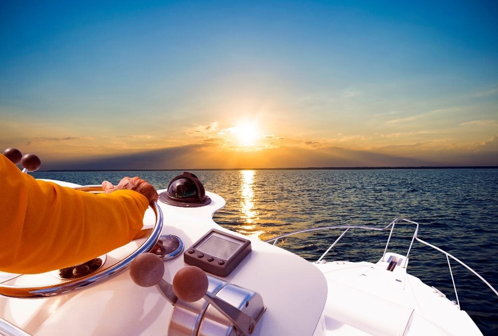 Hand of captain, who is wearing an orange jacket, on steering wheel of motor boat in the blue ocean in piece about CIOs managing expectations of CEOs.