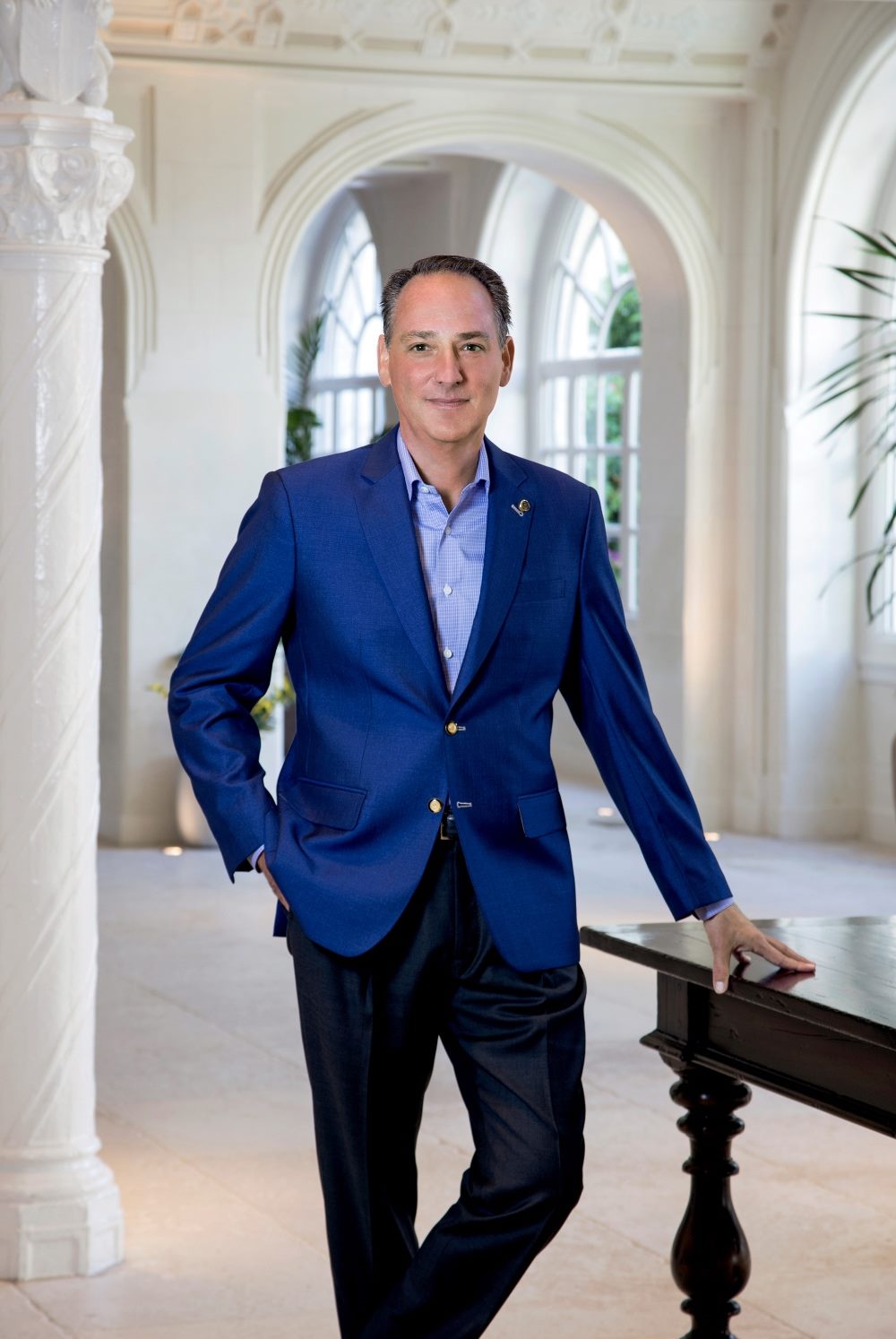 Portrait of five-star hotelier, Danile Hostettler standing by a table.