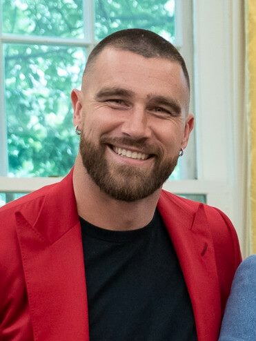 Head shot of Travis Kelce wearing a red suit jacket and black T-shirt sporting a beard and smiling in piece about branding strategies and brand authenticitty.