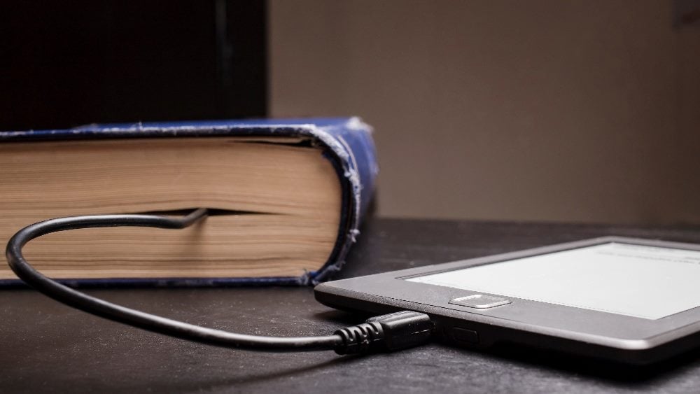 A well worn copy of a blue book connected to an e-readers device suggesting "progress" in piece about the impact of AI in marketing.