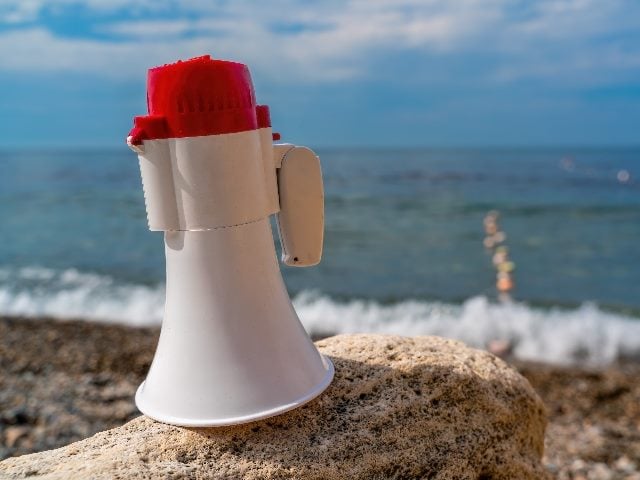  Red and White loudspeaker with the backdrop of a blue sea at a beach.
