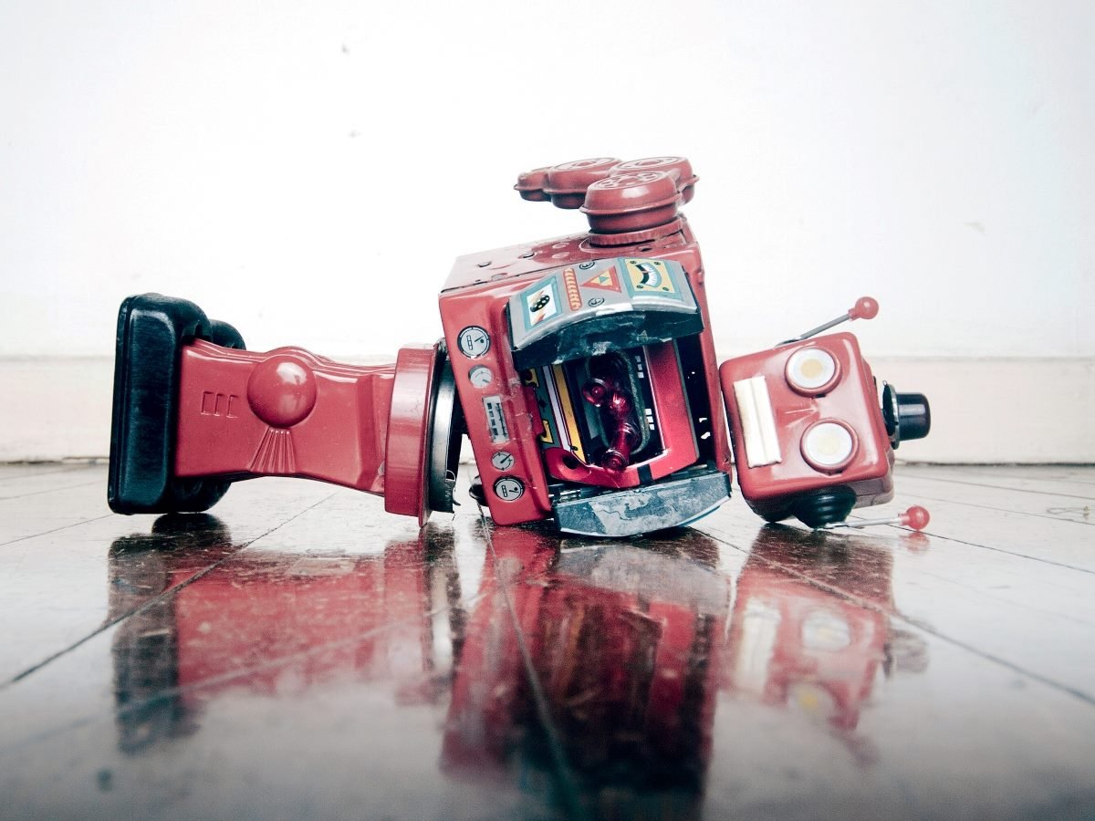 A vintage red toy robot lies broken and toppled over on a wooden floor, symbolizing AI or technology failure.