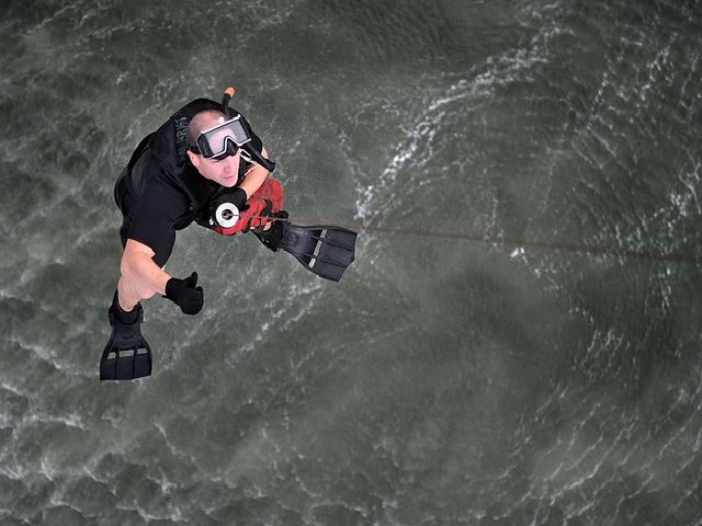 navy search and rescue diver being lowered into the ocean by a line from a helicopter