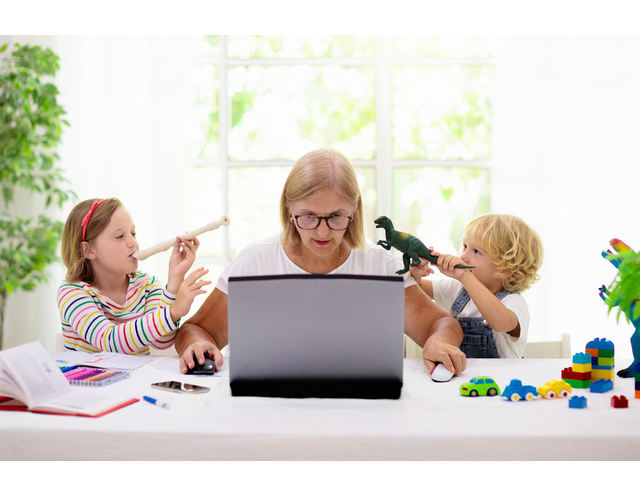 a woman flanked by two kids raising toys to her ear as she tries to work on a laptop.