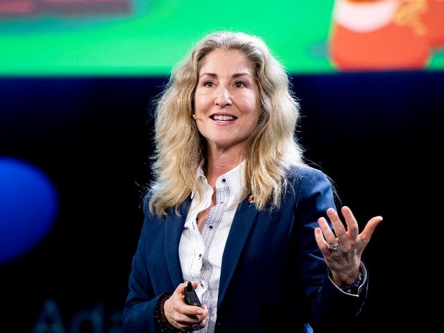 Tiffani Bova wearing a blue suit jacket and white shirt appears on stage delivering a presentation with the colors red, green and blue in the background in piece about leadership and CX and EX.