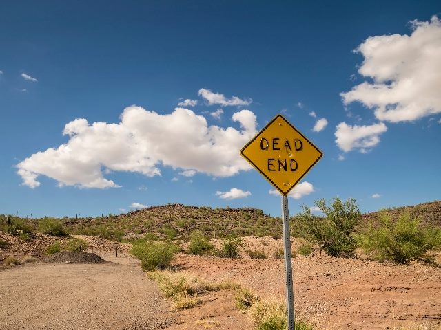 Road sign with bullet holes and peeling letters in Arizona desert. 