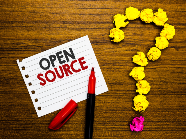Text on paper spelling out open source next to pen and crumpled papers forming question mark wooden background. Open source questions concept