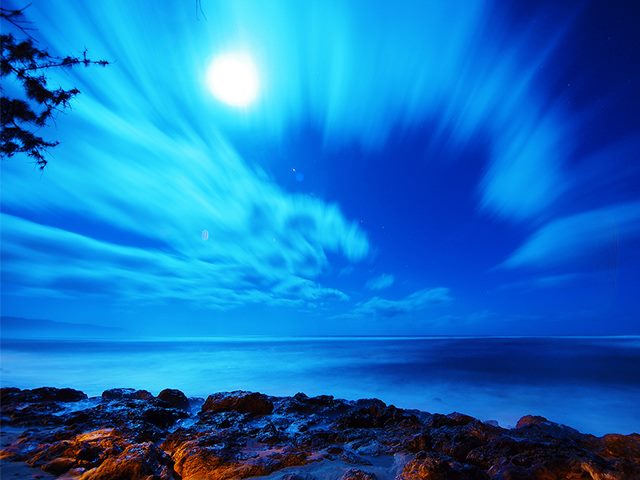 Full moon lighting up a bright nighttime sky by the ocean. 