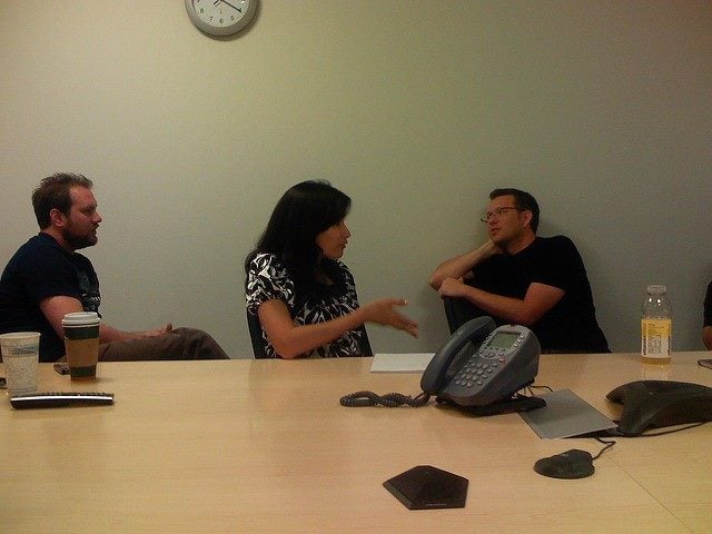 Woman and two men at a conference table discussing business.