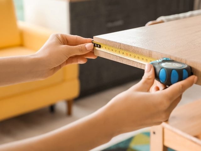  Young woman, showing just her hands, taking measures of table in kitchen.