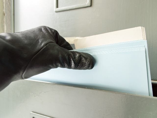 A hand wearing a black leather glove getting into a paper file cabinet.