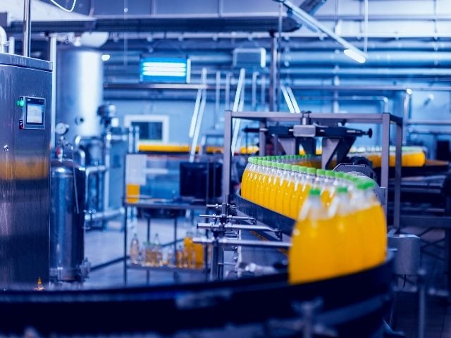 Beverage factory interior, with bottles of a beverage colored orange going through a factory conveyor automation belt.  