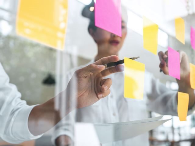 Young creative team professional using post it notes on a glass wall writing a CX alignment plan