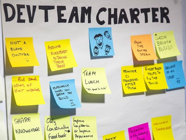 White poster board that has "Dev Team Charter" written on it surrounded by stickies with messages for team strategy on each. Modern DevOps must embrace agile deployment methods, according to Murthy Peri of SapientRazorfish.