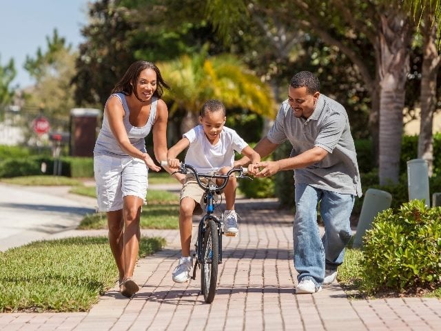 Woman and man help a boy ride his bicycle. 