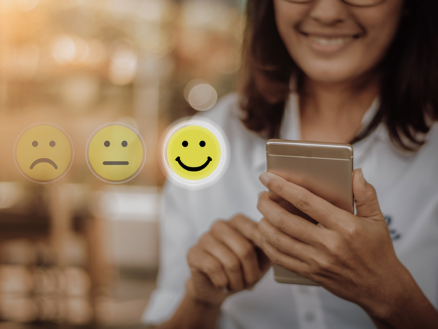 Businesswoman interacting with social media platform, pressing face emoticon on smartphone.