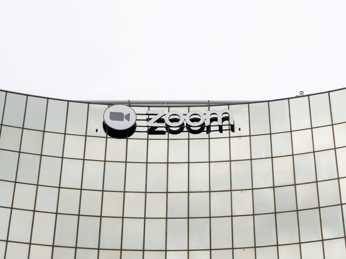 Zoom logo displayed on the curved glass exterior of a modern office building against a gray sky.