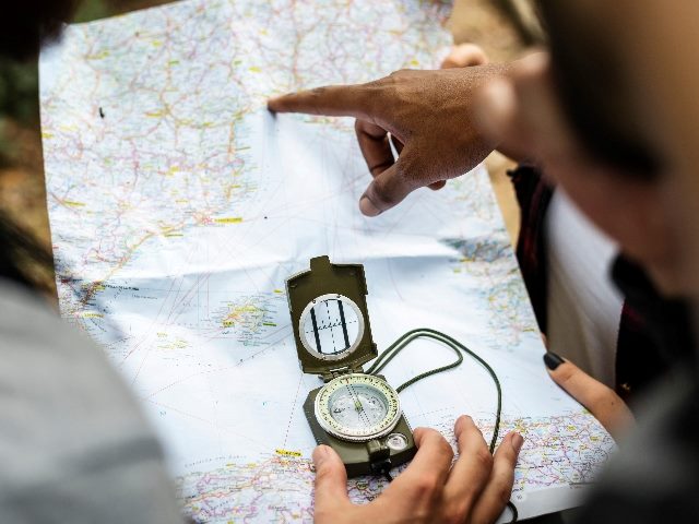 Three different hands on a map as one of the hands holds a compass. 