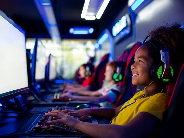  Group of kids in game room sitting and playing computer video games. 