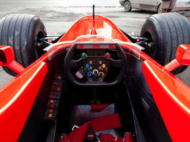 Cockpit and steering wheel view of red Ferrari racing sports cars for Formula 1 on the street near the garage box.