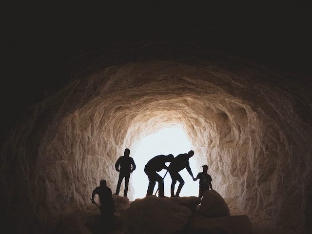 silhouettes of people in a cave making their way towards the light
