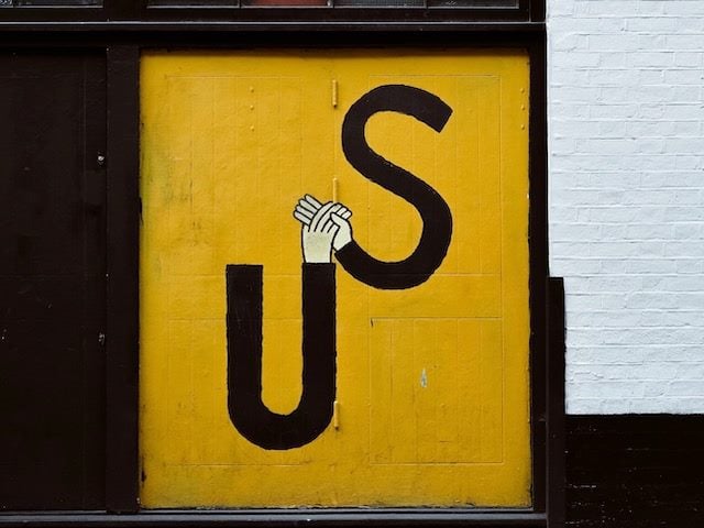 street art: the word "Us" with hands at the end of the letter U clasping a hand at the end of letter S