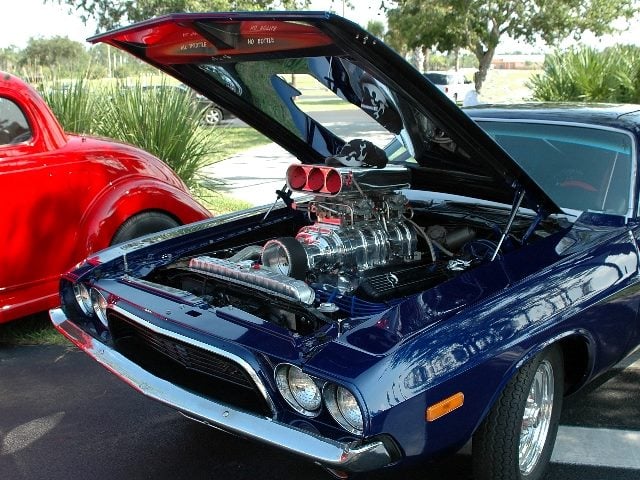 A dark blue vintage muscle car with the hood up at a car show displays a stock car motor suggesting looking under the hood at generative AI history. 