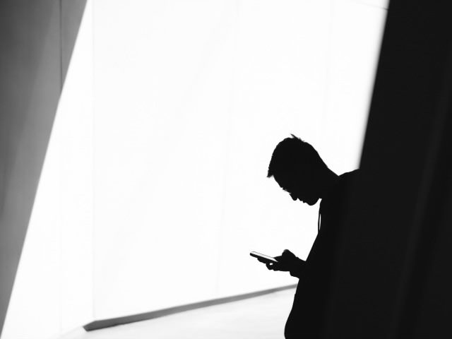 a man, leaning against a wall and reading on his phone