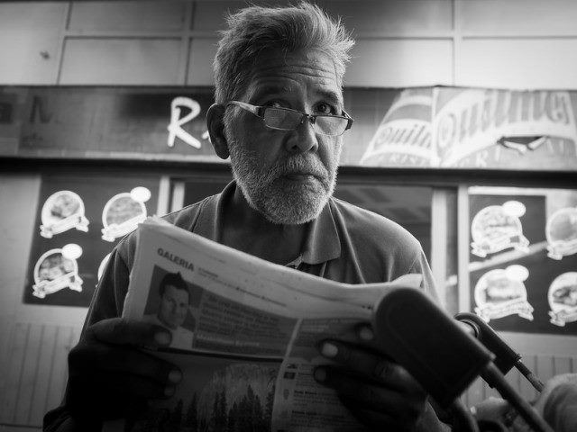Man sitting down and holding a newspaper looking up and ahead.