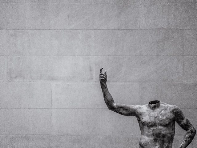 a headless statue with arm raised in a gallery
