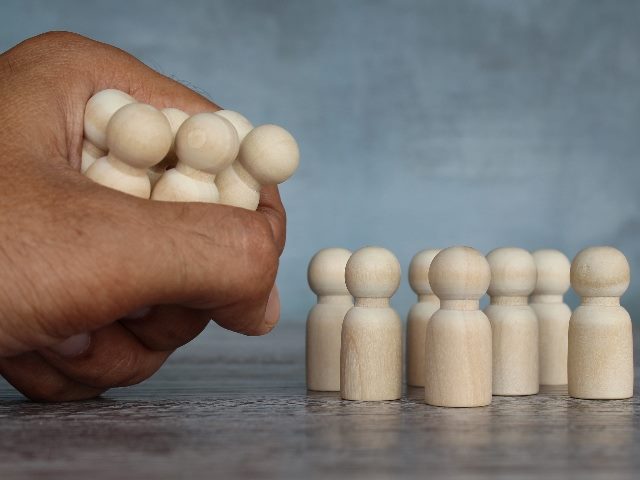 A hand grabbing several wooden people figures, from a stack of wooden people figures, representing a downsizing concept.