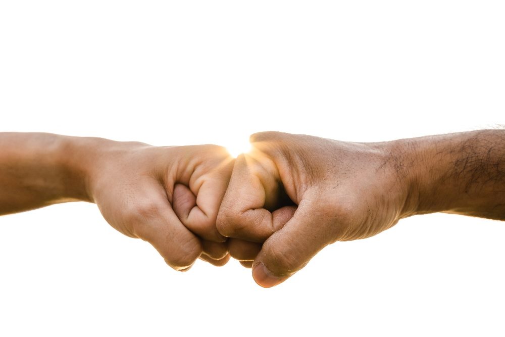 Two hands come together in a fist bump with the sun in the background in piece about real-time data.
