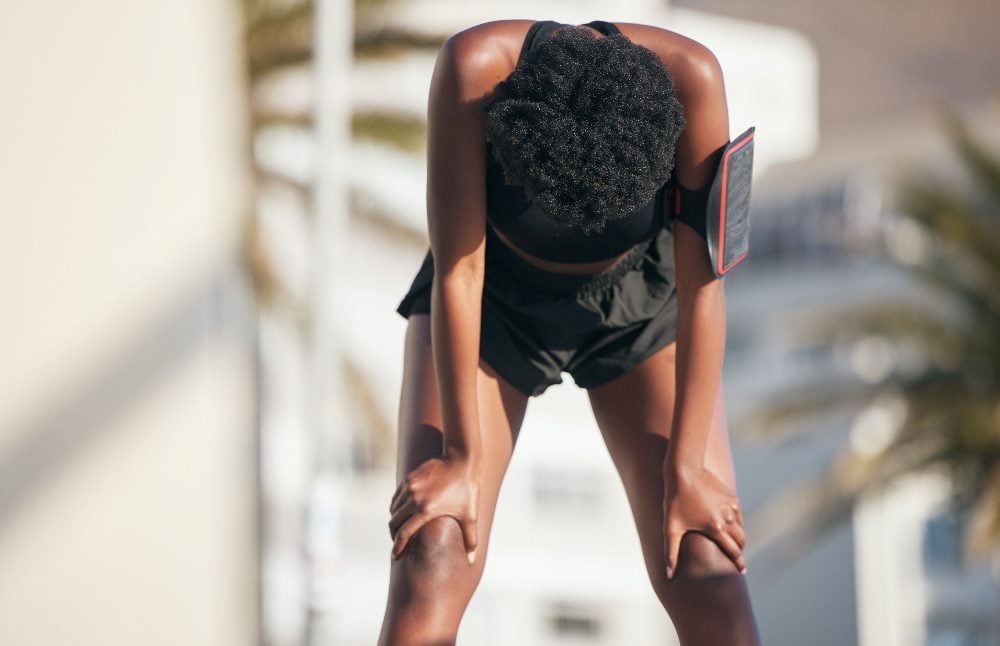 A fatigued runner wearing black exercise clothes leans over with their hands clasping the legs just above the knee in piece about customer survey fatigue.
