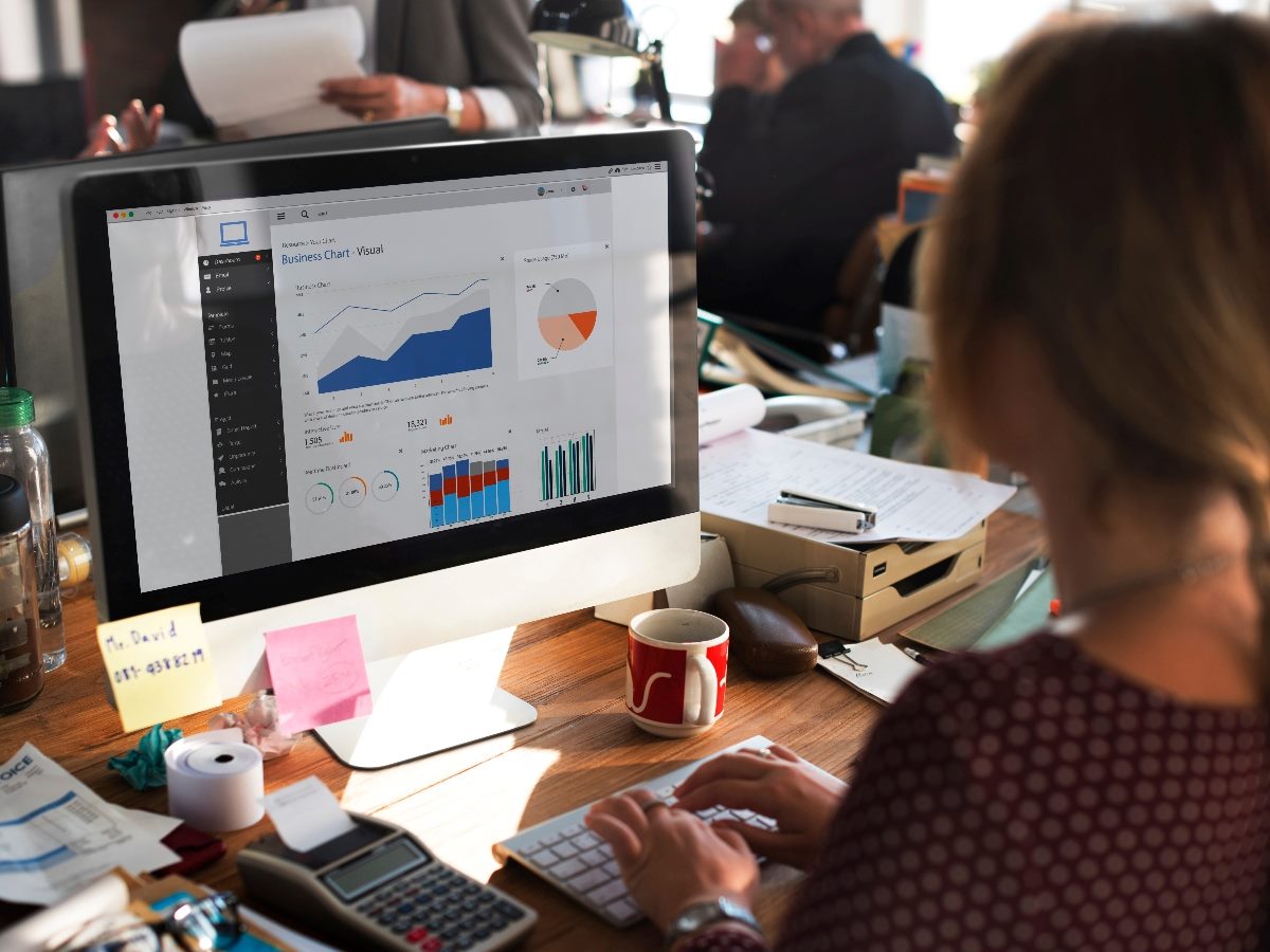 Business professional analyzing operational reporting dashboard with charts and graphs on a desktop computer, highlighting digital experience analytics and AI-driven insights.