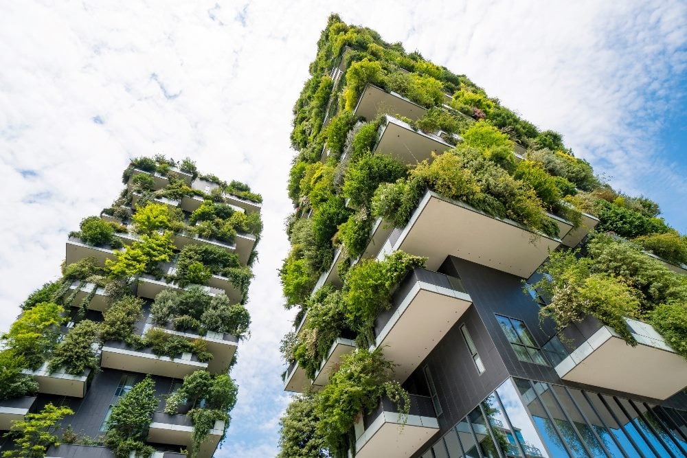 Two skyscrapers covered in green vegetation named Vertical Forest in Milan with a blue sky with white clouds overhead in piece about sustainable website design.